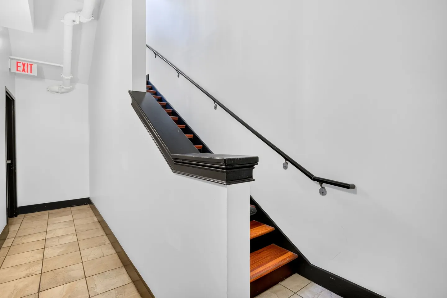 Indoor hallway with tile flooring leading to a wooden staircase with black railings and white walls.