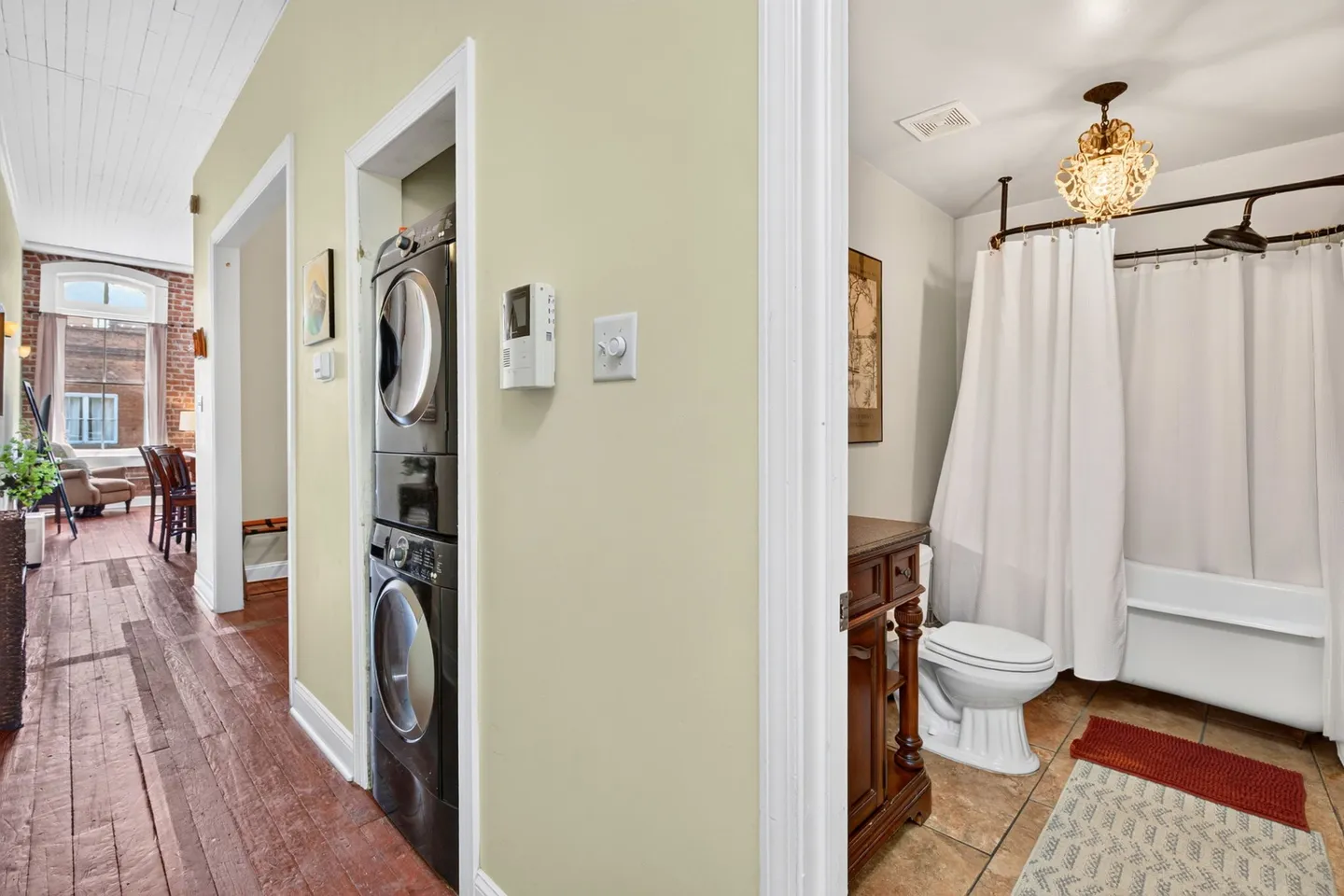 Hallway featuring a stacked washer and dryer in a closet opening, with a view of a bathroom to the right and a living area straight ahead.