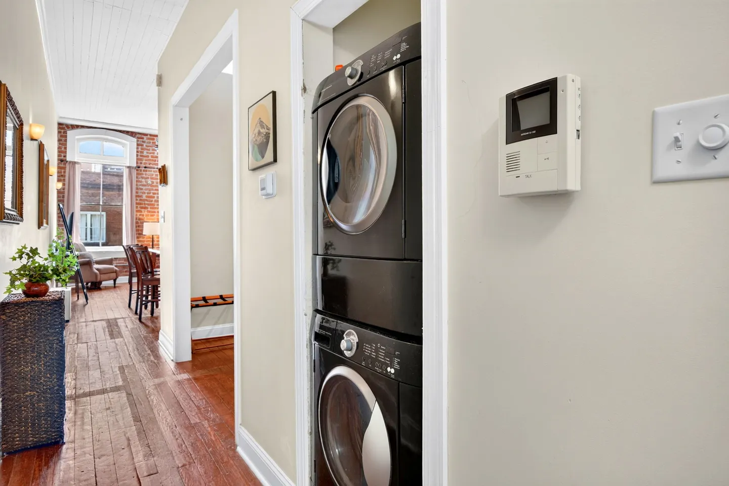 Hallway featuring a stacked black washer and dryer set in an alcove next to wood floors.