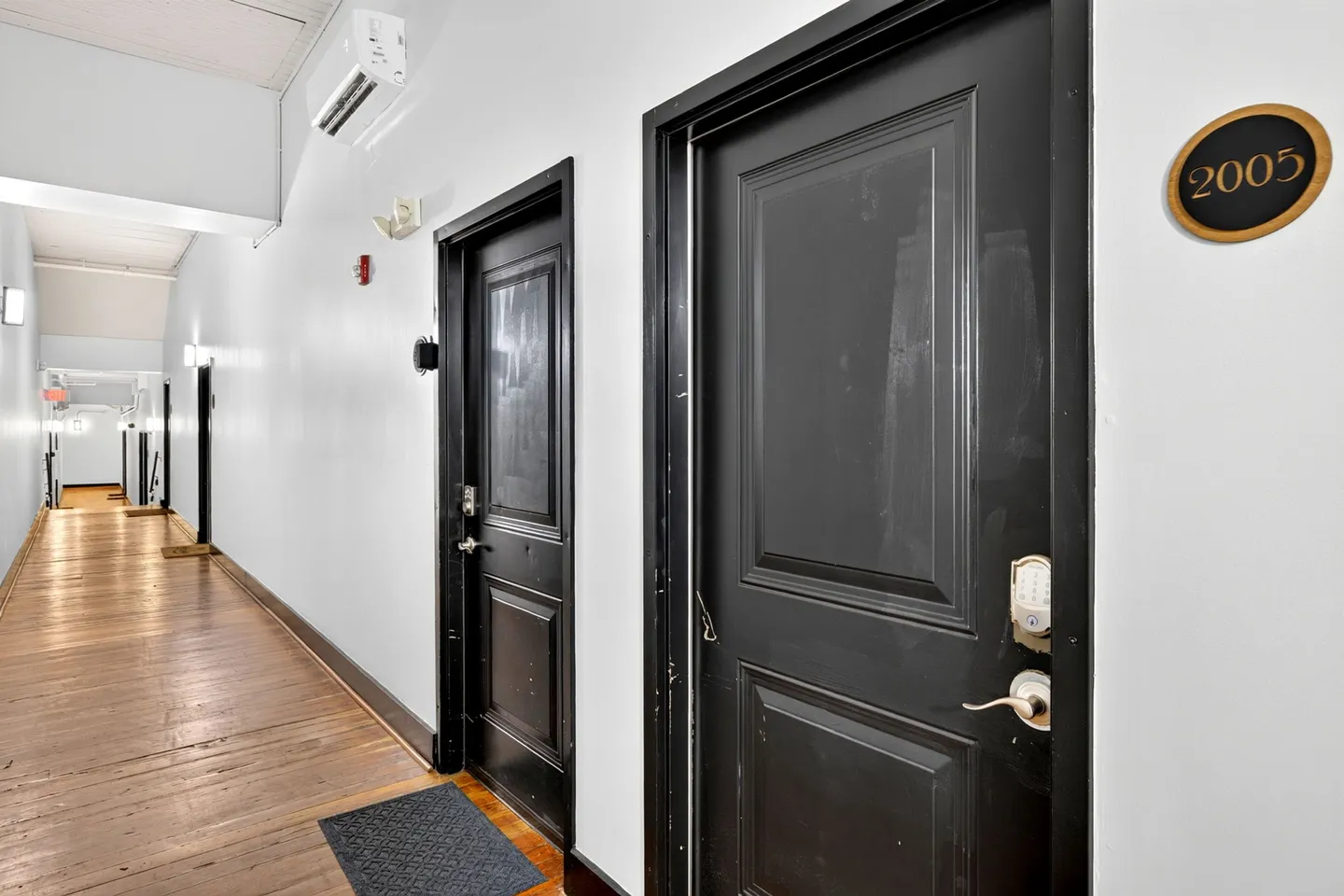 Indoor hallway with dark entry doors, numeric keypad locks, and wood-plank flooring.