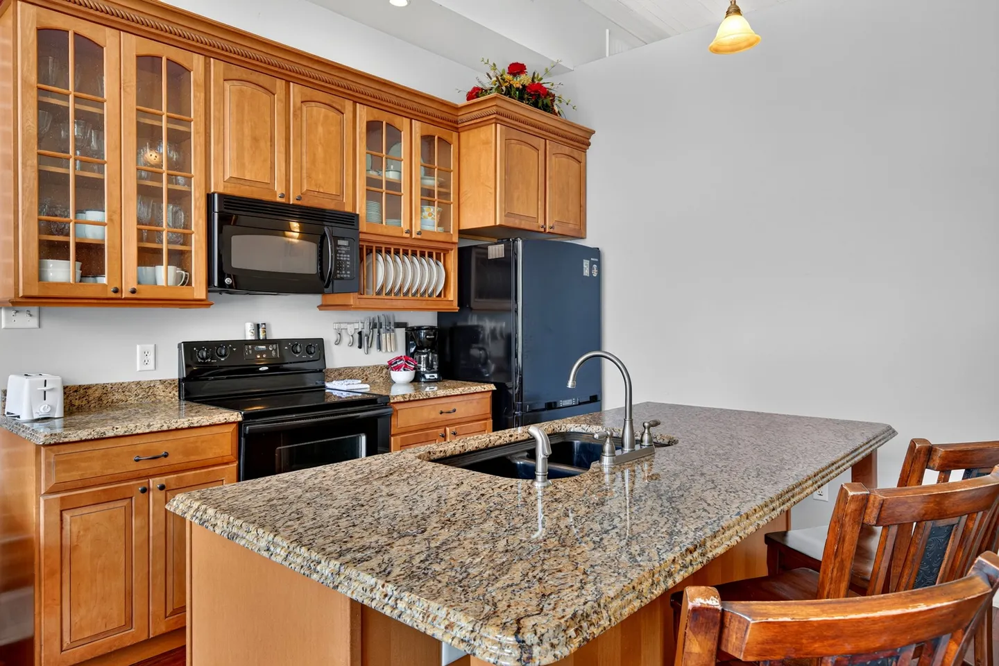 Kitchen with wooden cabinetry, speckled granite countertops, a center island with sink, and black appliances.