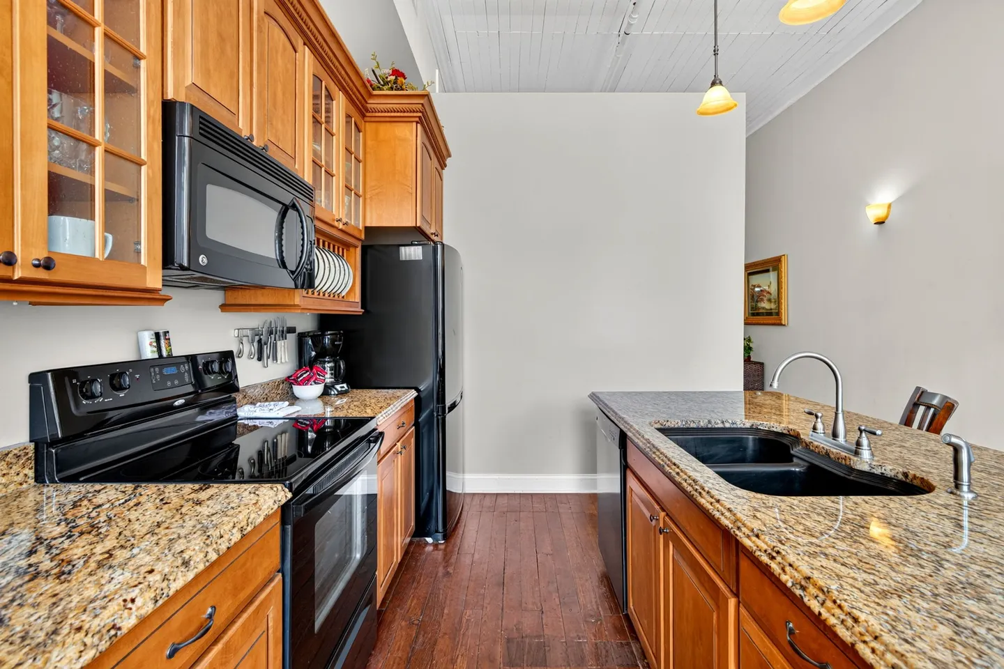 Kitchen interior featuring wood cabinets, speckled granite countertops, black appliances, and dark wood flooring.