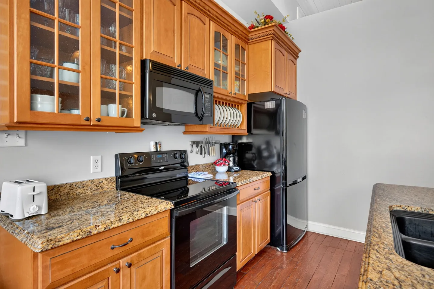 Kitchen with wooden cabinetry, speckled granite countertops, a black electric range, mounted microwave, and a black refrigerator.