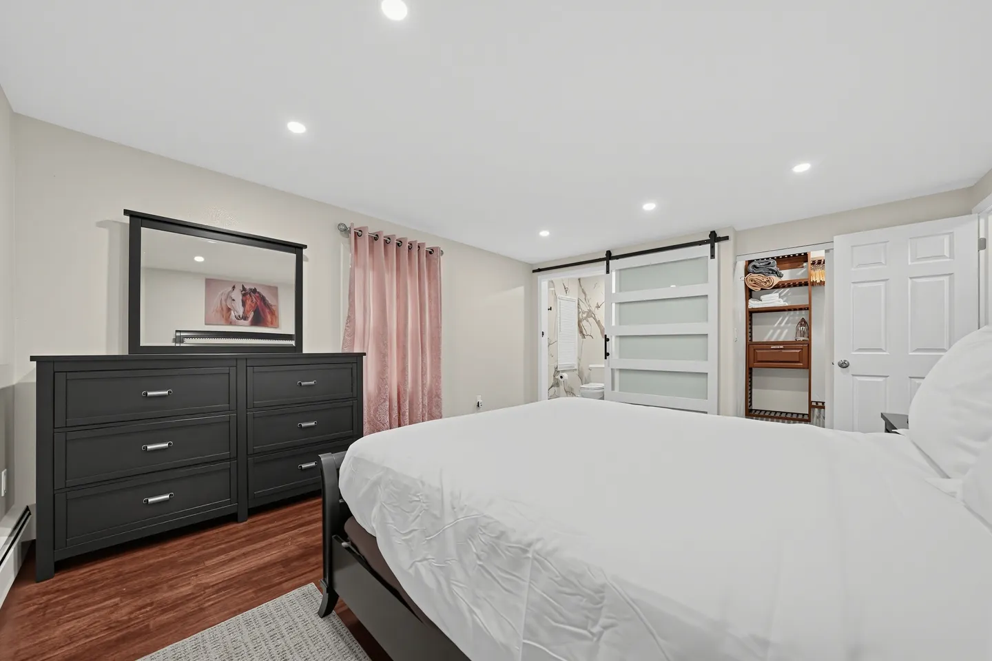 Bedroom with a white-linened bed, dark dresser with mirror, and sliding barn door leading to an en suite bathroom and open closet.