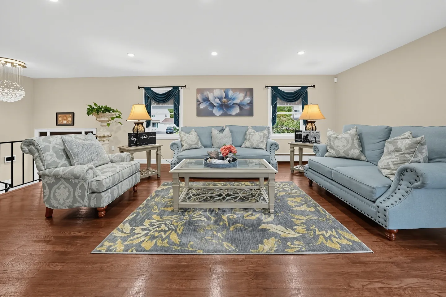 Living room featuring light blue upholstered couches, an armchair, a glass coffee table, and patterned area rug over wood-style flooring.