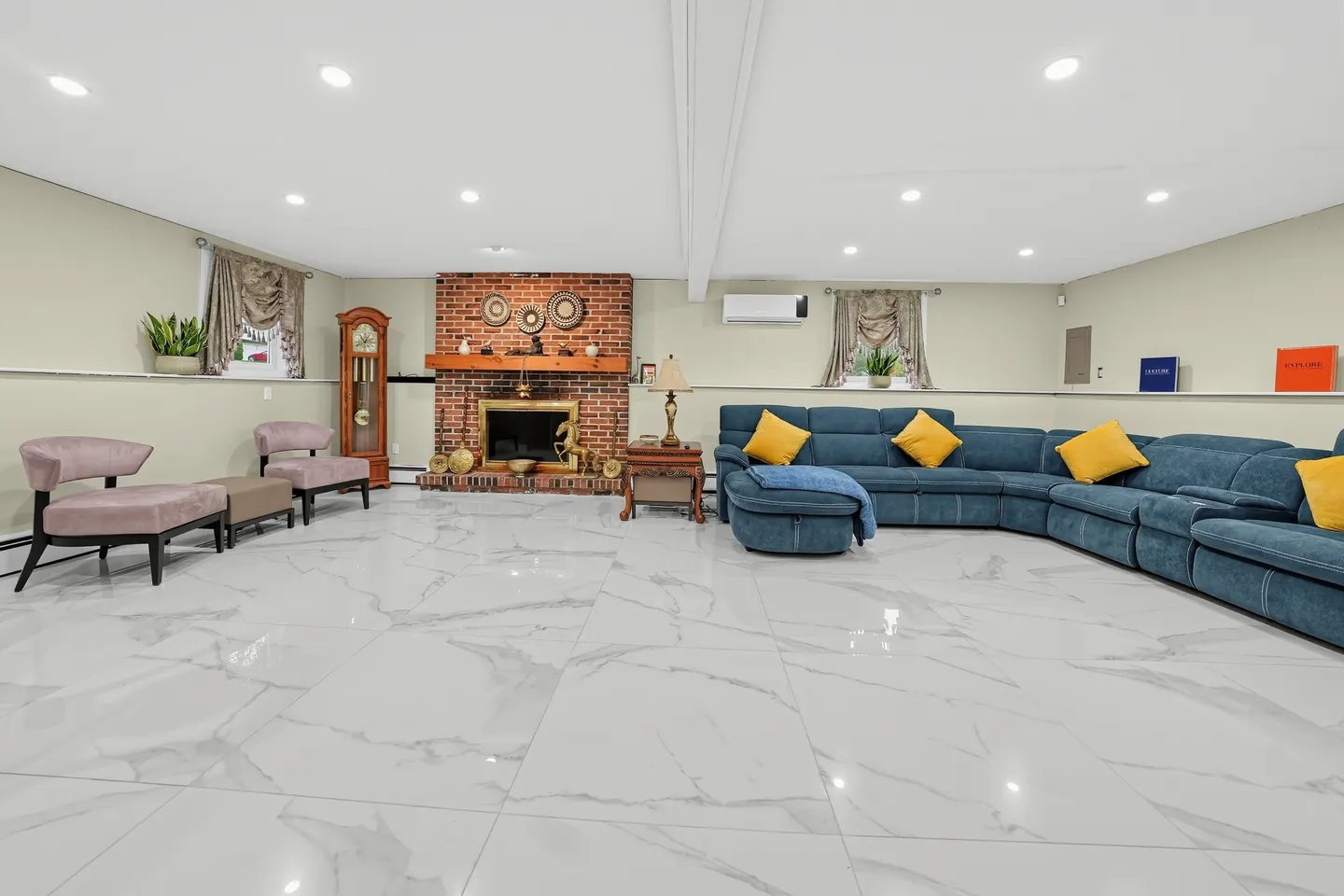 Spacious living room featuring glossy marble-style floor tiles, a brick fireplace, and a large blue sectional sofa.