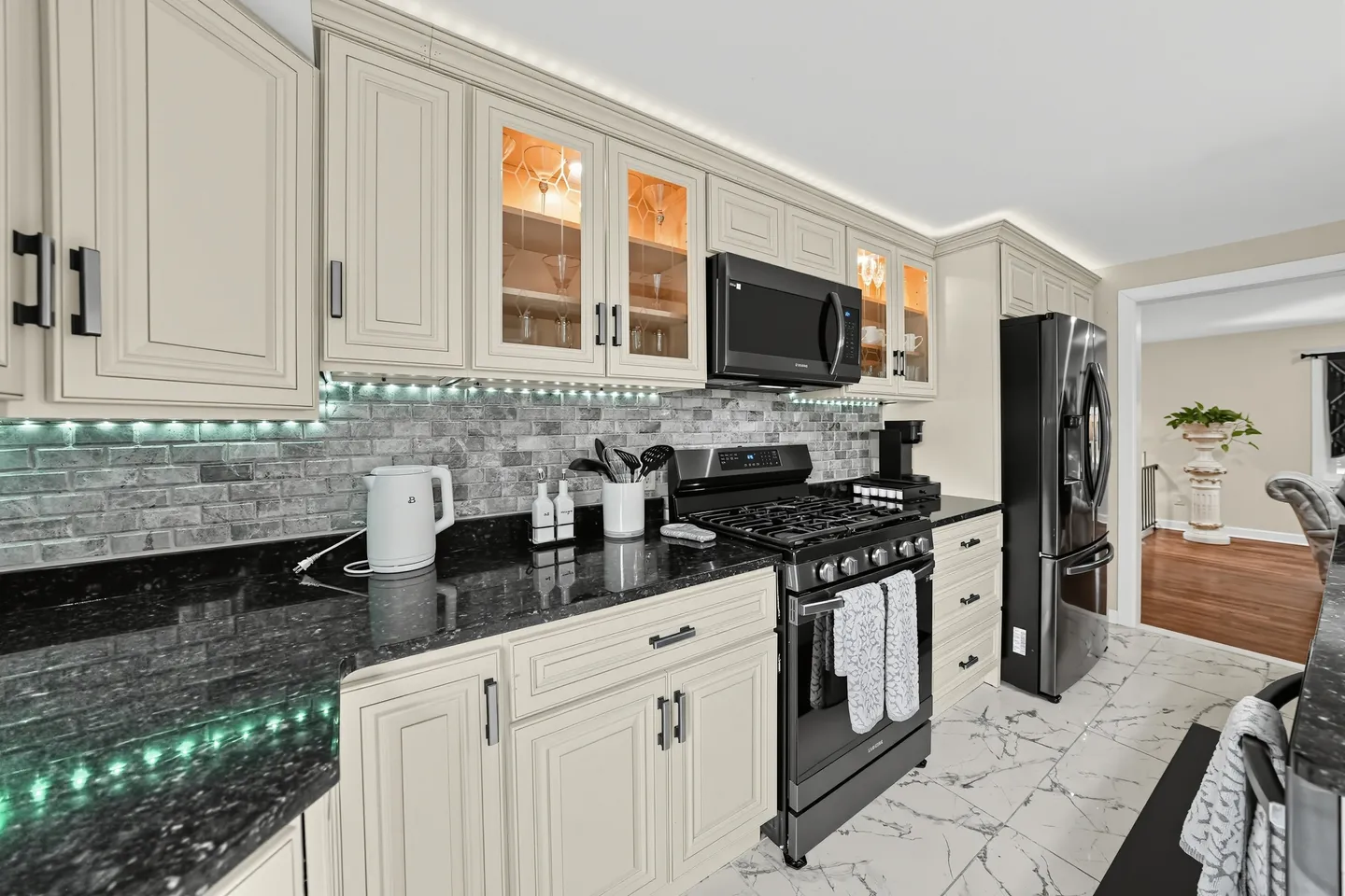 Kitchen featuring light cabinetry, dark countertops, a brick-style backsplash with under-cabinet lighting, and black appliances.
