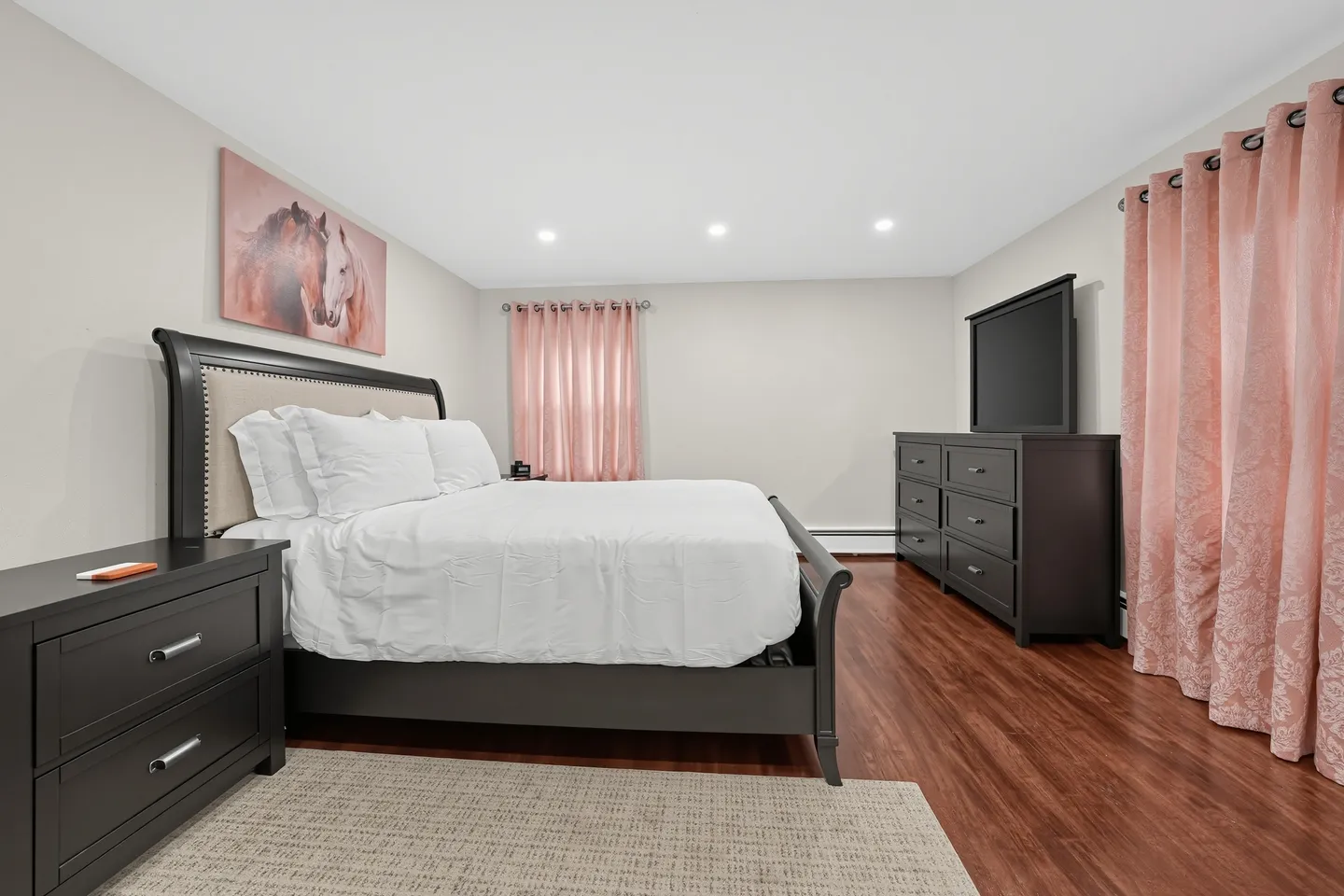 Bedroom with dark wood sleigh bed, matching furniture, wood-look floors, and pink curtains.