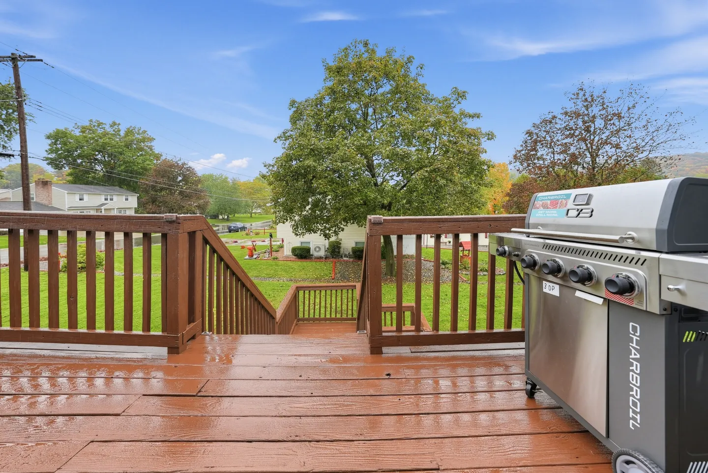 Elevated wooden deck with stairs leading down to a green yard, featuring a Char-Broil gas grill on the right.