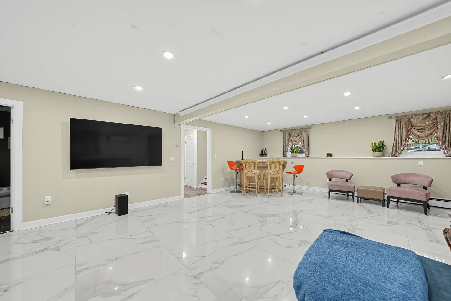 Spacious finished basement with polished marble-look tile floors, a wall-mounted flat-screen TV, and a bar area with seating.