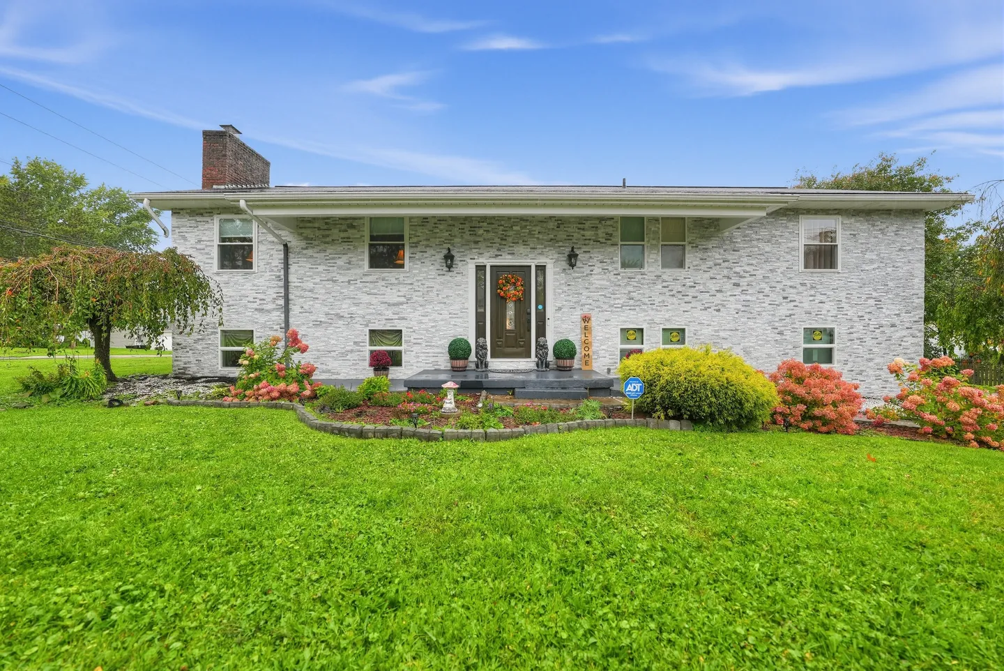 Front exterior of a split-level home with a gray stone facade, front lawn, and landscaped flower bed.