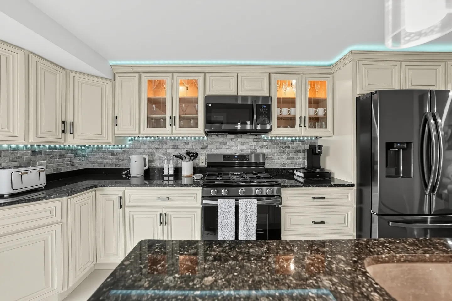 Kitchen with cream-colored cabinetry, dark speckled granite countertops, a tiled backsplash, and stainless steel and black appliances.