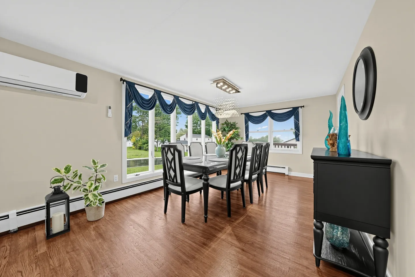 Dining room with a dark dining table, cushioned chairs, hardwood floors, large windows with blue valances, and a chandelier.