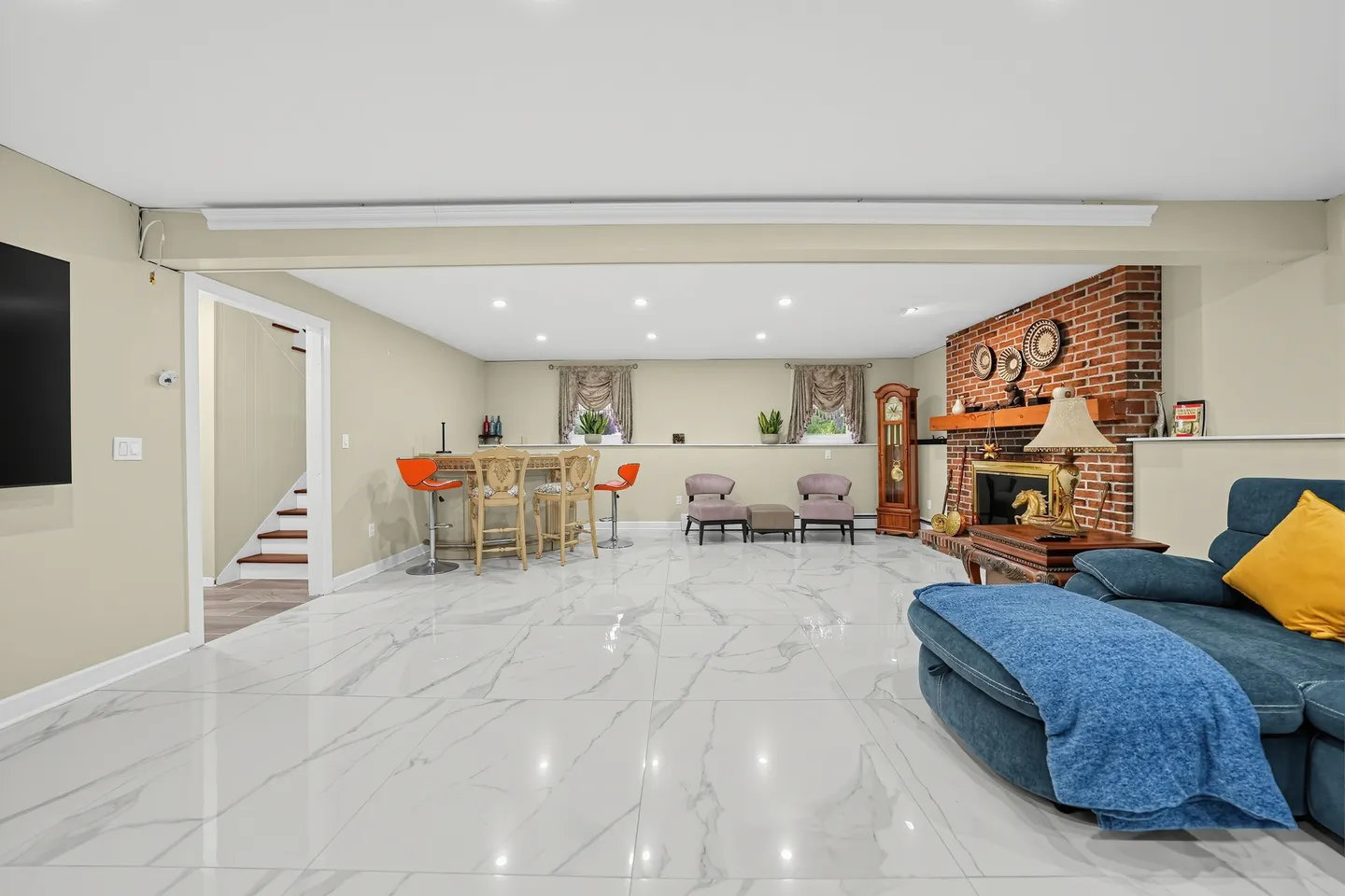 Spacious finished basement living area with glossy marble-look tile floors, a brick fireplace, a wooden bar with barstools, and a blue sofa.
