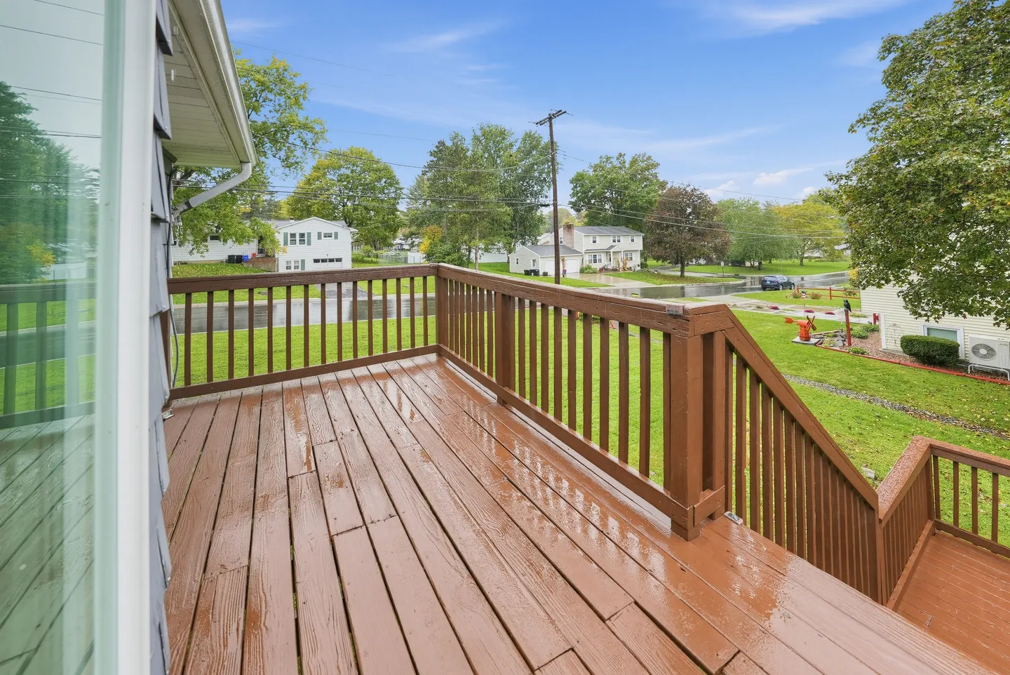 Elevated wooden deck with railings overlooking a grassy lawn, street, and nearby neighborhood homes.