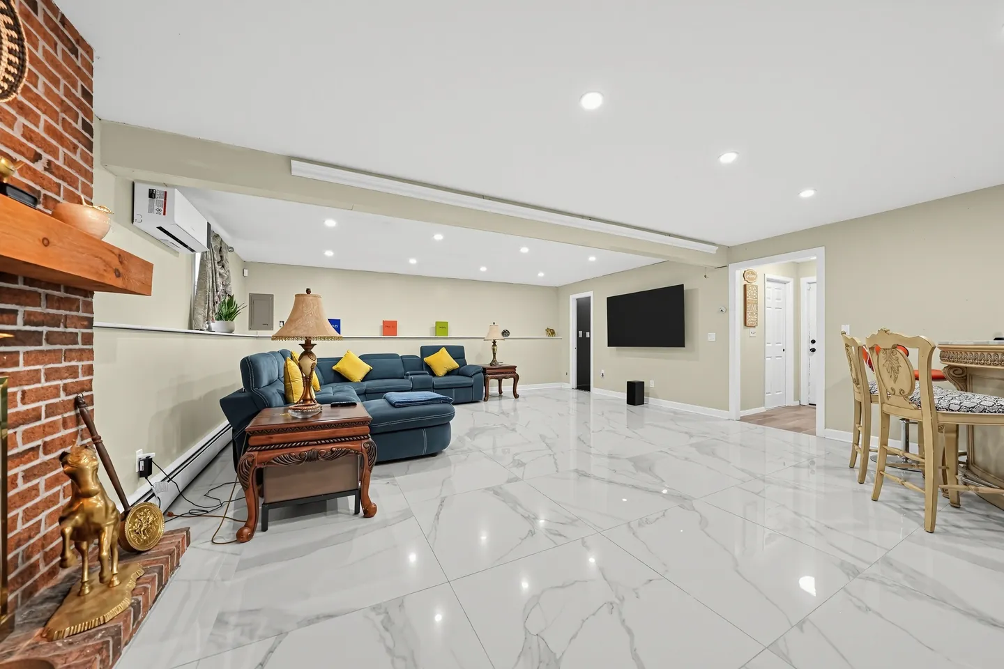 Spacious indoor living room with glossy marble-style tiled floors, a brick fireplace, a blue sectional sofa, a wall-mounted TV, and bar seating.