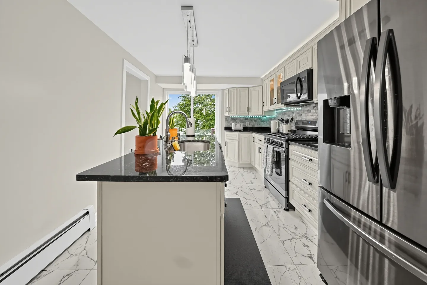 Modern kitchen with a black granite island, white cabinetry, stainless steel appliances, and marble-patterned tile flooring.