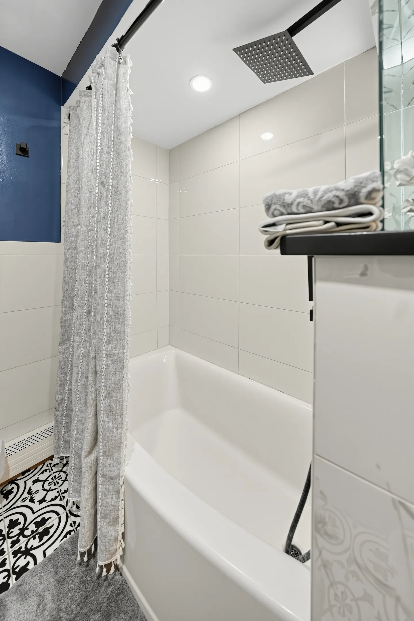 Bathroom featuring a white bathtub and shower with large white wall tiles, an overhead square rain showerhead, and a gray shower curtain.