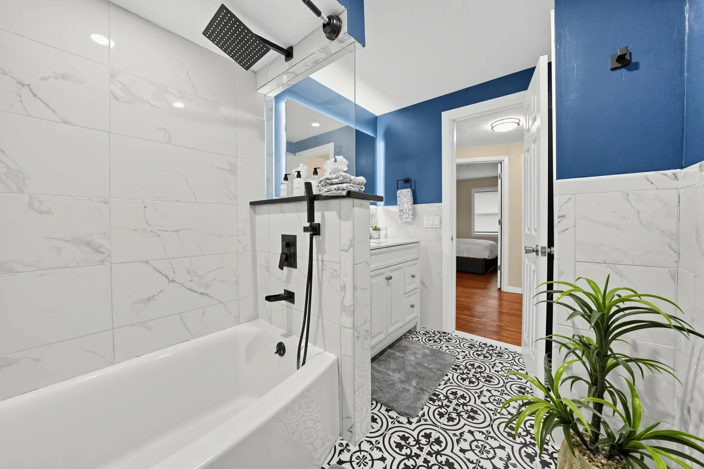Bathroom with white marble-patterned tile, matte black shower fixtures, a white vanity, and patterned tile flooring.