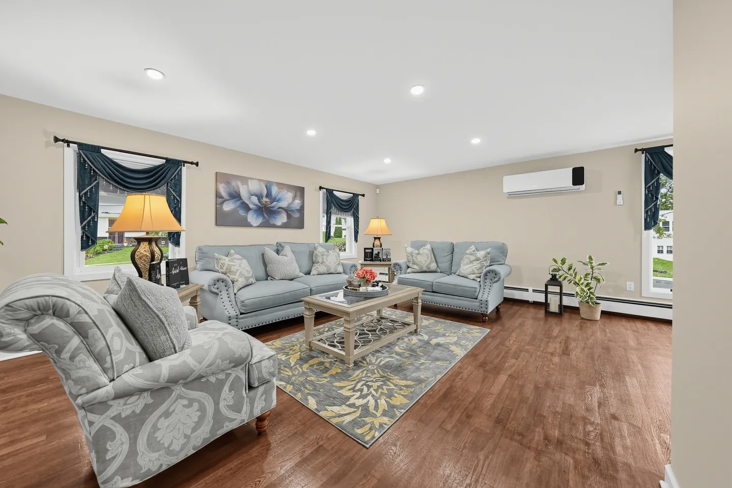Living room with wood-style flooring, light blue sofas, an armchair, coffee table, and recessed ceiling lights.