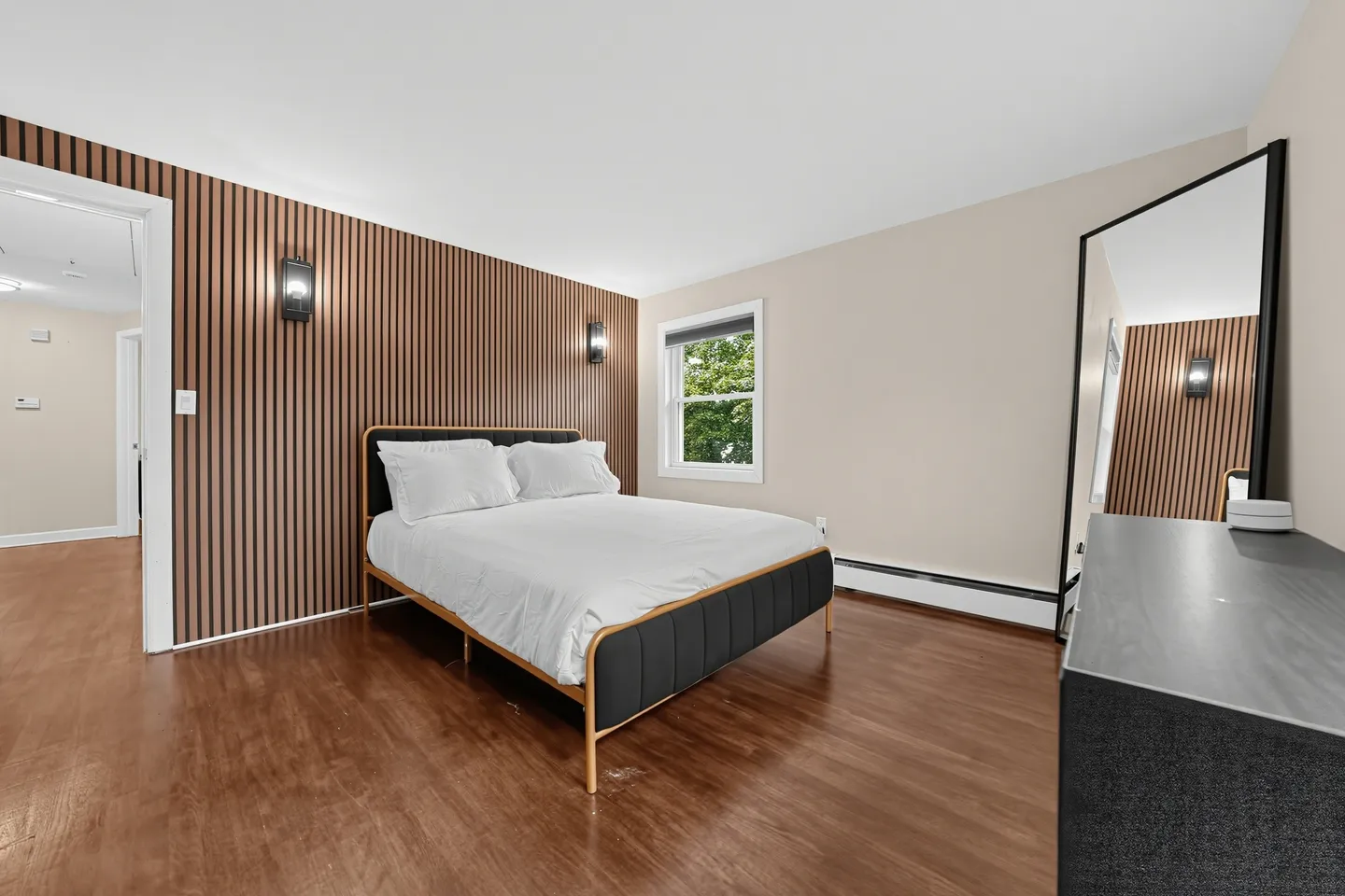 Bedroom with wood-paneled accent wall, bed with black upholstered frame, and a full-length leaning mirror.
