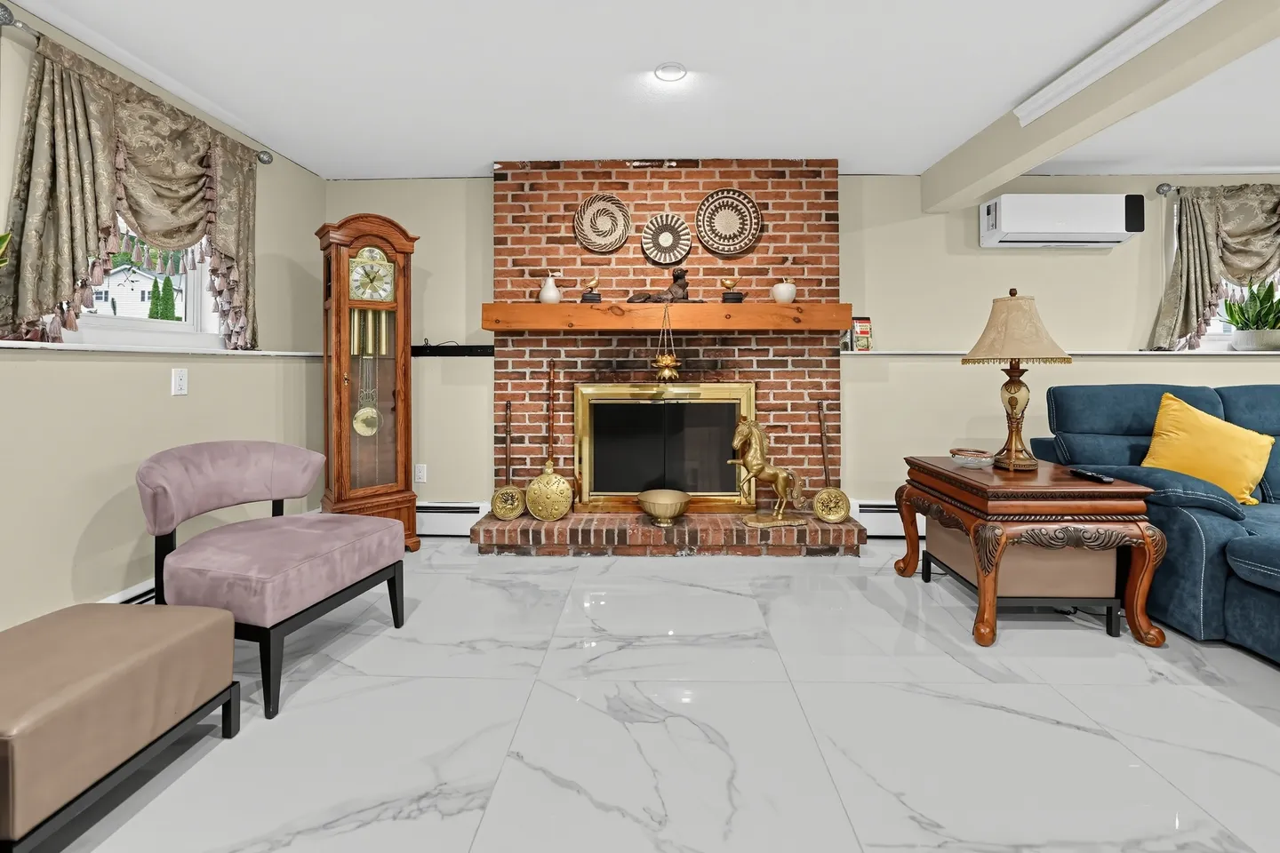 Living area featuring a brick fireplace with a wood mantel, polished marble-style tile flooring, and assorted seating.