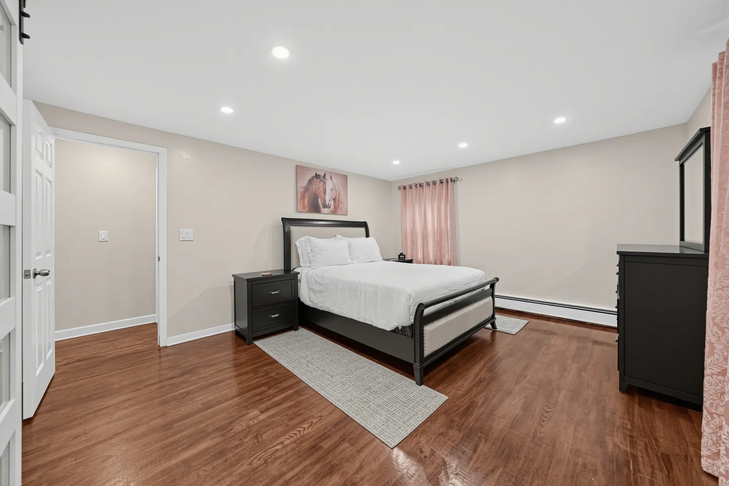 Spacious bedroom with wood-look flooring, a dark-framed bed, matching nightstand, and dresser.