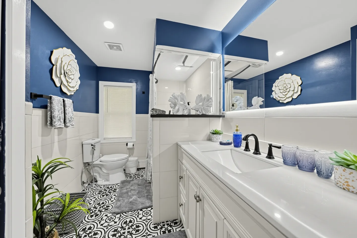 Bathroom featuring a white vanity with black fixtures, blue upper walls, white tiled lower walls, decorative black and white floor tiles, a toilet, and a walk-in shower.