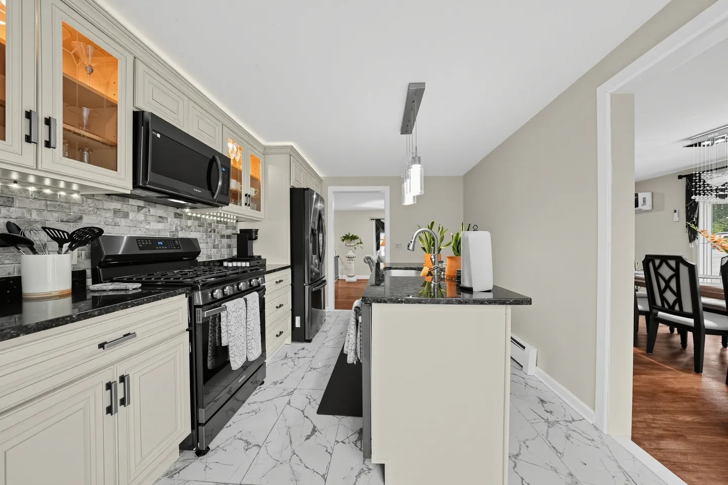 Kitchen with marble-patterned tile flooring, light cabinetry, dark countertops, black appliances, and a kitchen island.
