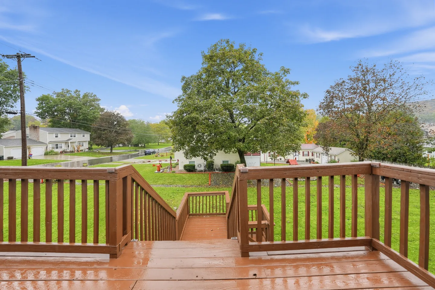 Elevated wooden deck with stairs leading down to a green lawn and neighborhood view.