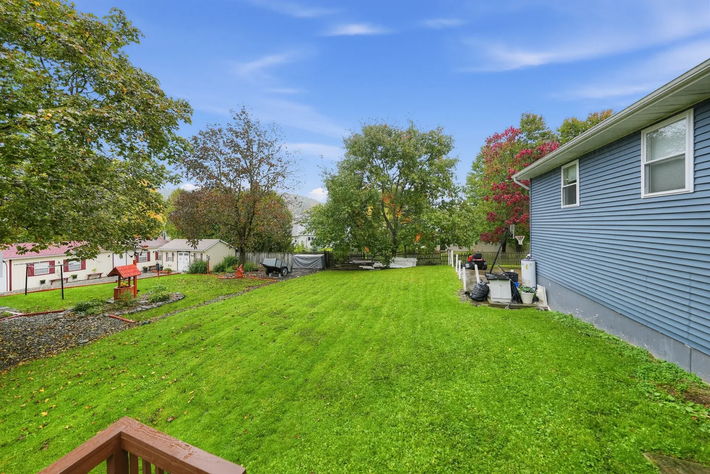 A wide view of a spacious grassy backyard bordered by trees and neighboring properties, with the side of a blue house visible.