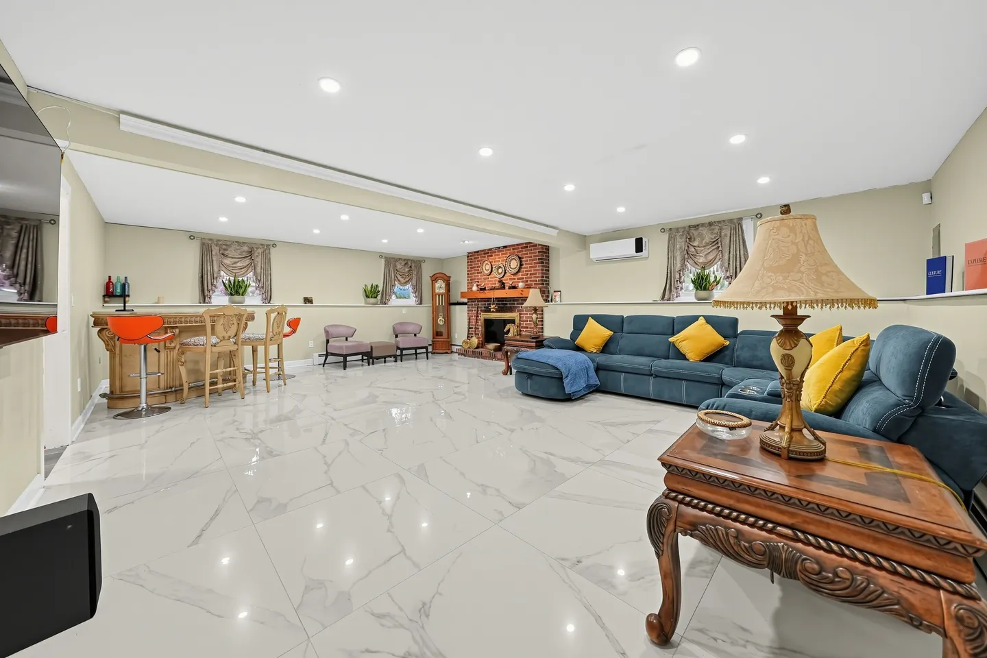 Spacious finished basement living area with tiled floors, a sectional sofa, brick fireplace, and wet bar.