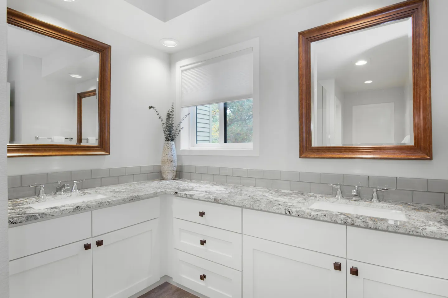 Bathroom double vanity with an L-shaped granite countertop, white cabinets, and two wood-framed mirrors.