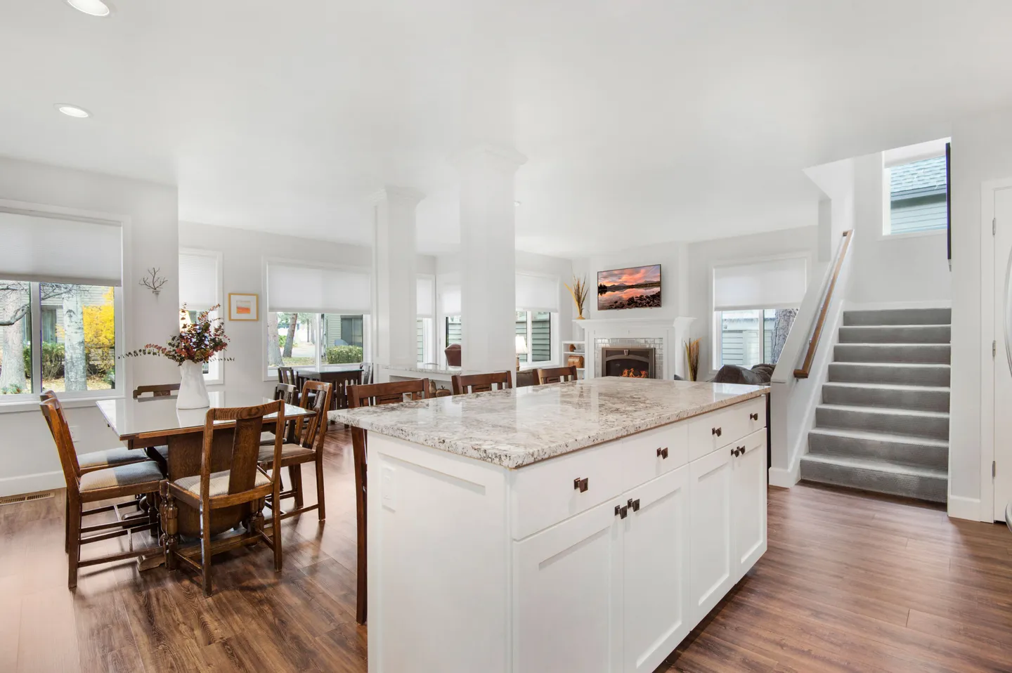 Open-concept living and dining area featuring a kitchen island with stone countertop, a wooden dining table, and stairs leading up.