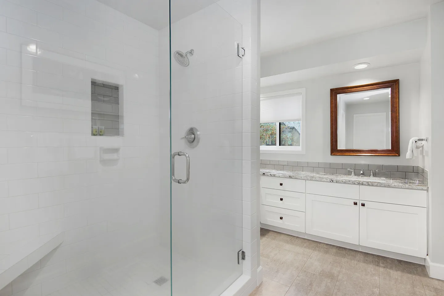 Bathroom featuring a walk-in glass shower with white subway tile, adjacent to a white vanity with marble-look counter and wood-framed mirror.