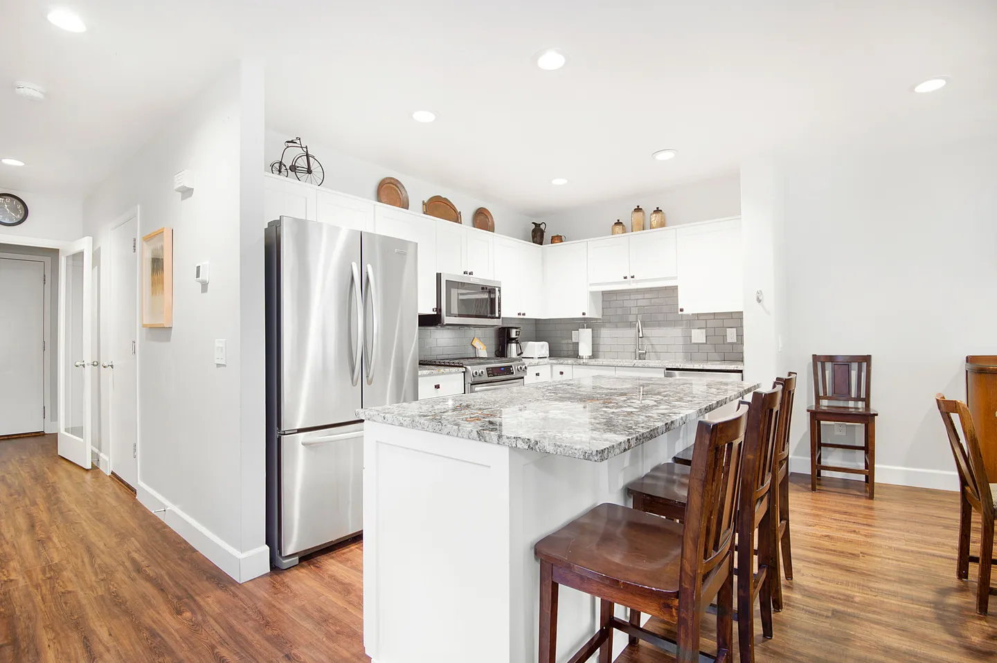 A brightly lit kitchen featuring a central island with wood barstools, white cabinets, and stainless steel appliances.