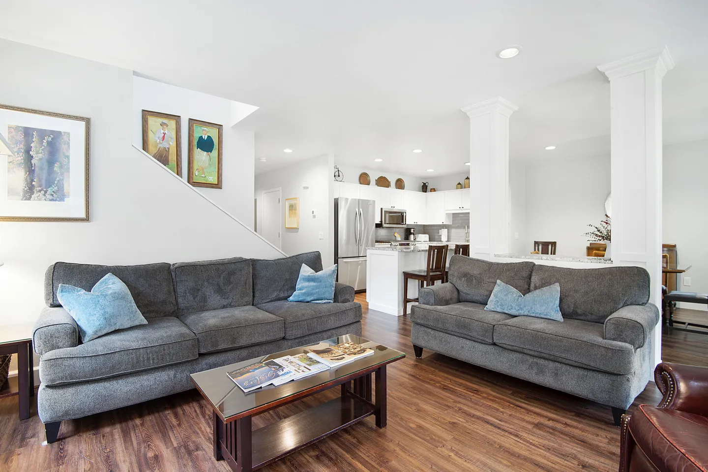 Open-concept living room with gray upholstered sofas, a coffee table, wood-style flooring, and a view into the kitchen.