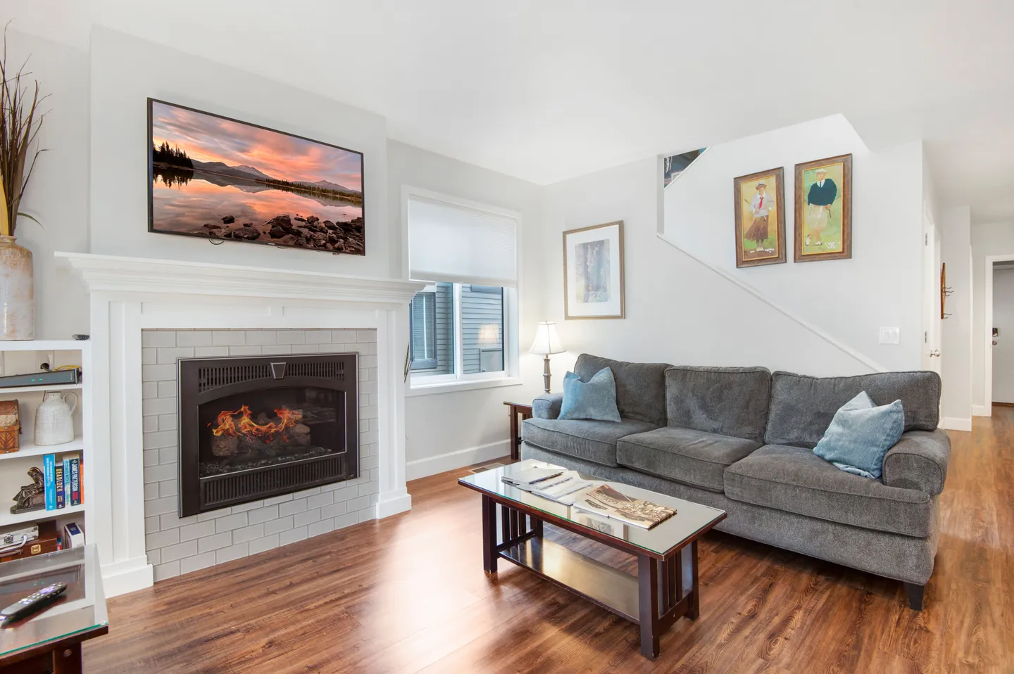 Living room with a gas fireplace, wall-mounted TV, grey sectional sofa, coffee table, and wood-look flooring.