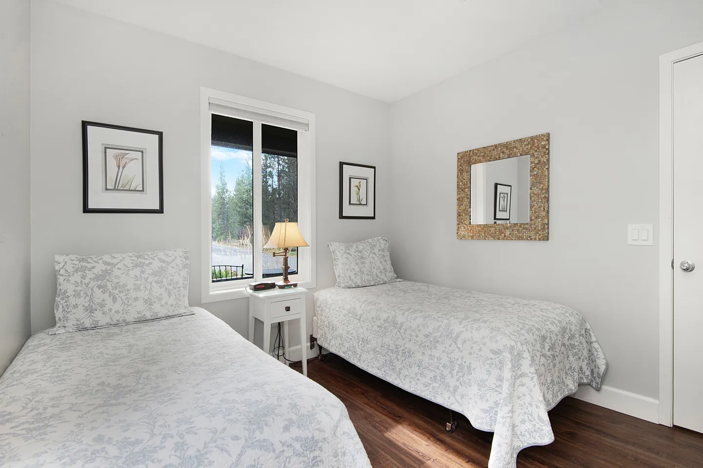 Bedroom with two twin beds dressed in floral patterns, a nightstand under a window, and wood-look flooring.