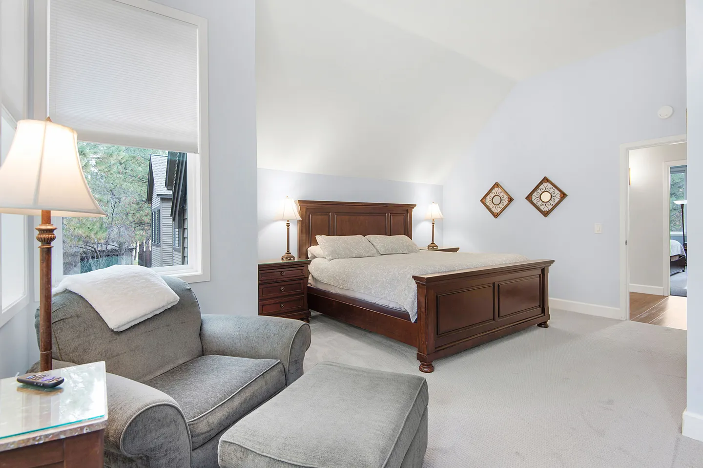 Spacious bedroom with a wooden bed, matching nightstands, a reading armchair with ottoman, and vaulted ceilings.