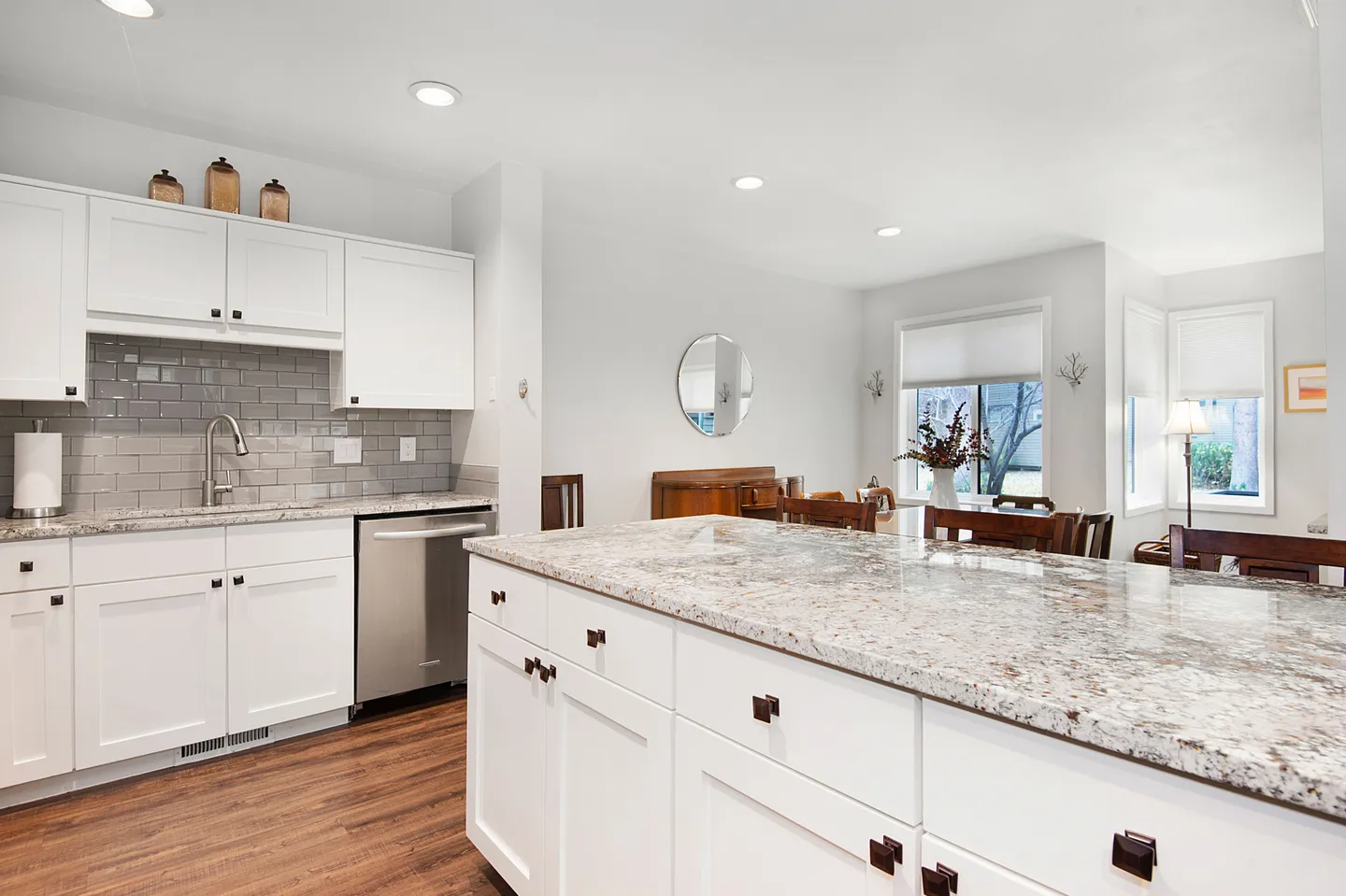Kitchen with large granite-topped island, white cabinets, grey tile backsplash, and an adjacent dining area.