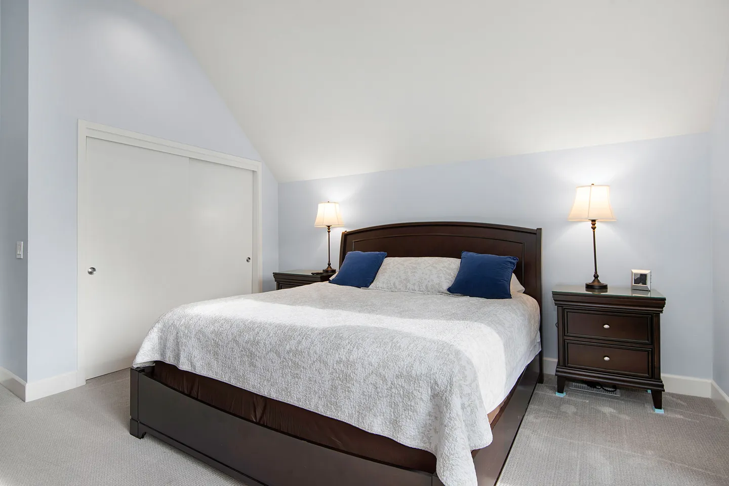 Bedroom with a dark wood bed frame, white bedding, matching nightstands with lamps, and a sloped ceiling.