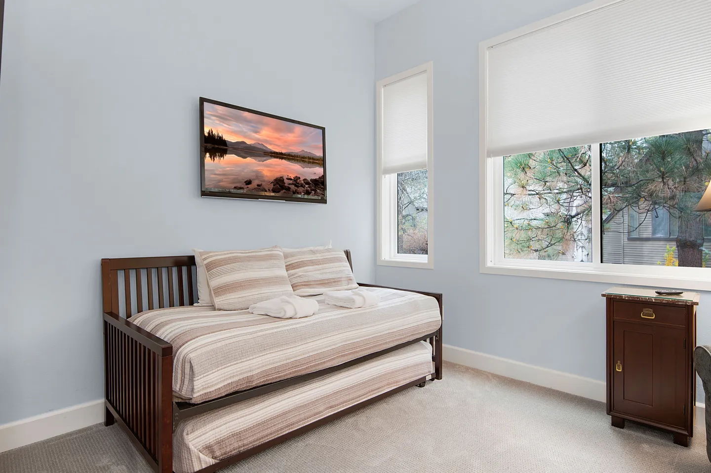 Bedroom corner featuring a wooden daybed with a trundle, striped bedding, a wall-mounted picture, and two windows.