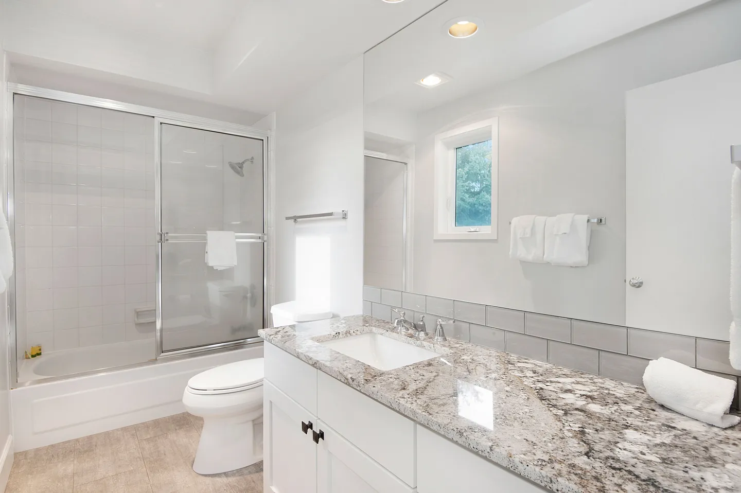 Bathroom with white cabinetry, granite countertop, toilet, and bathtub with sliding glass doors.
