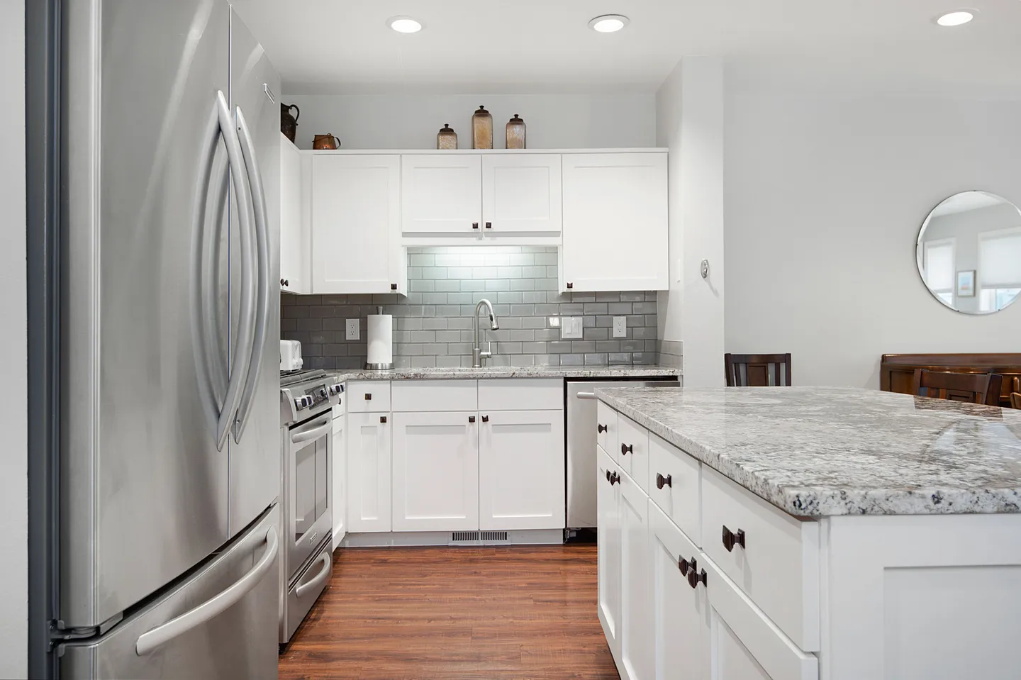 Kitchen with white cabinetry, stainless steel appliances, a kitchen island with stone countertops, and wood-look flooring.