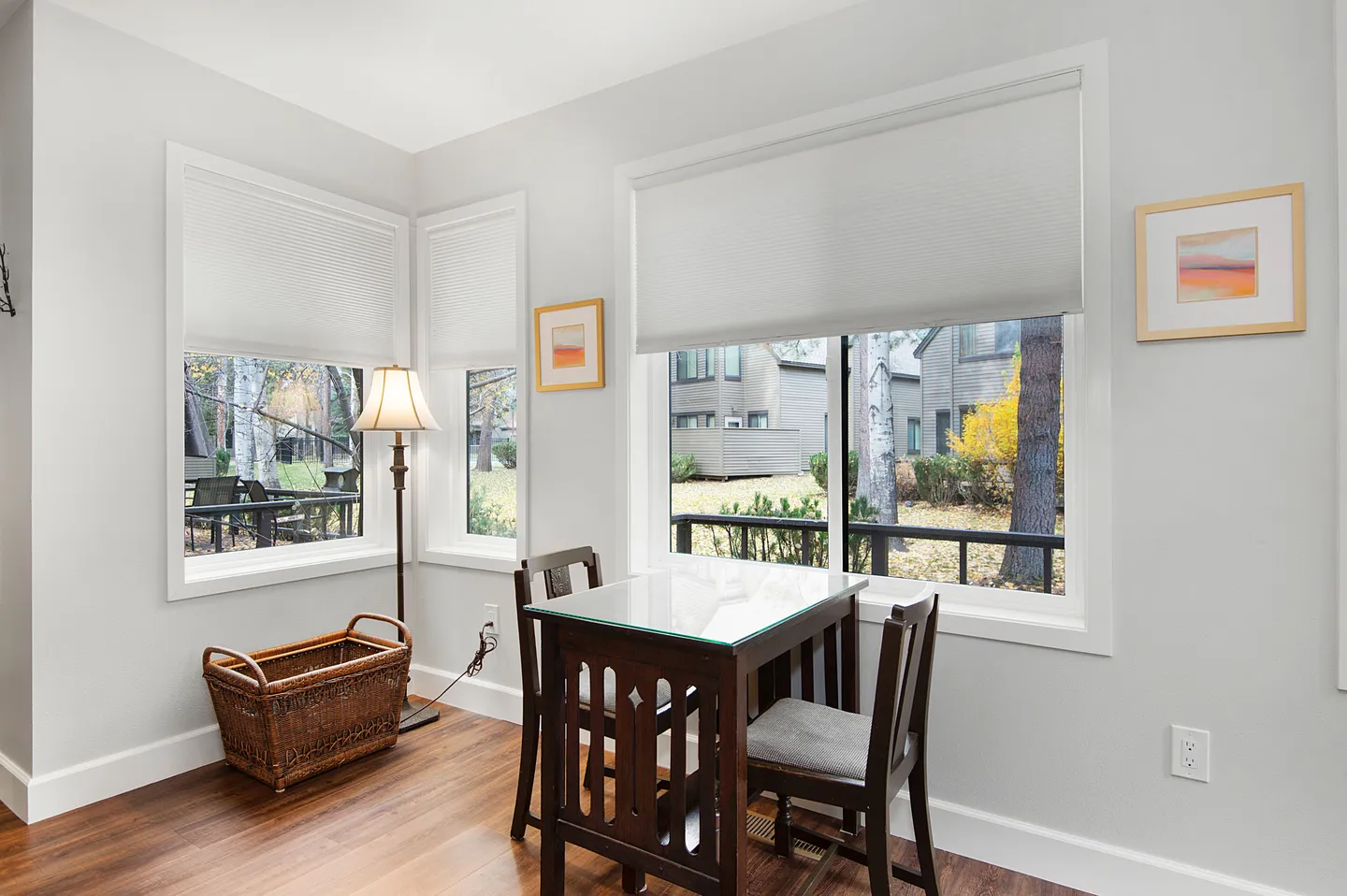 Dining nook with a small table, two chairs, and windows overlooking trees and neighboring buildings.