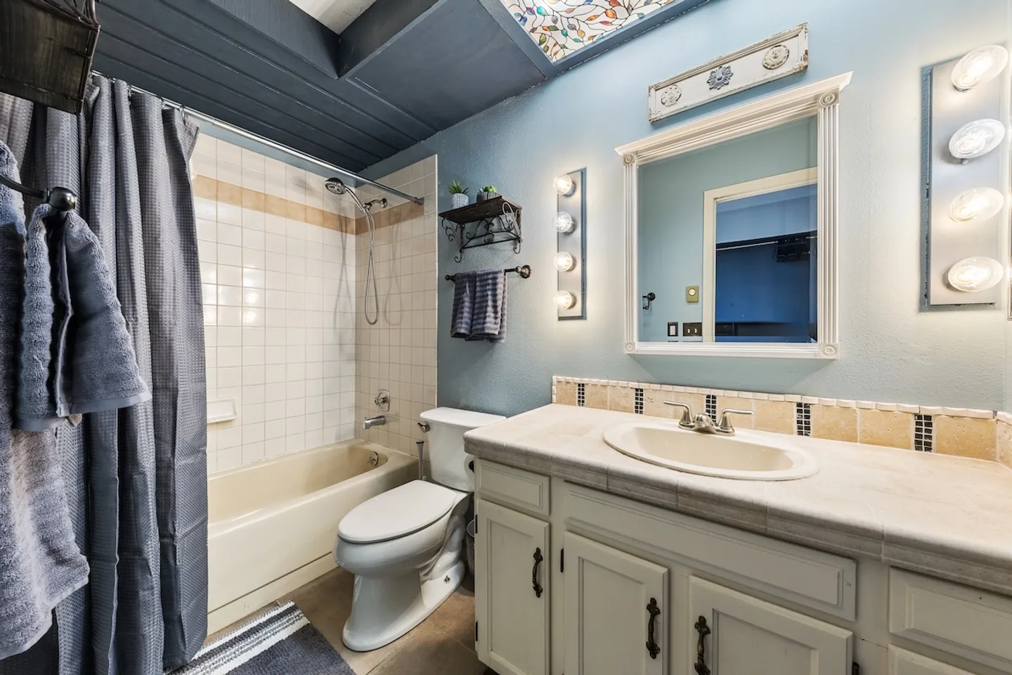 Bathroom featuring a vanity with a white framed mirror, a toilet, and a tiled shower-tub combination.