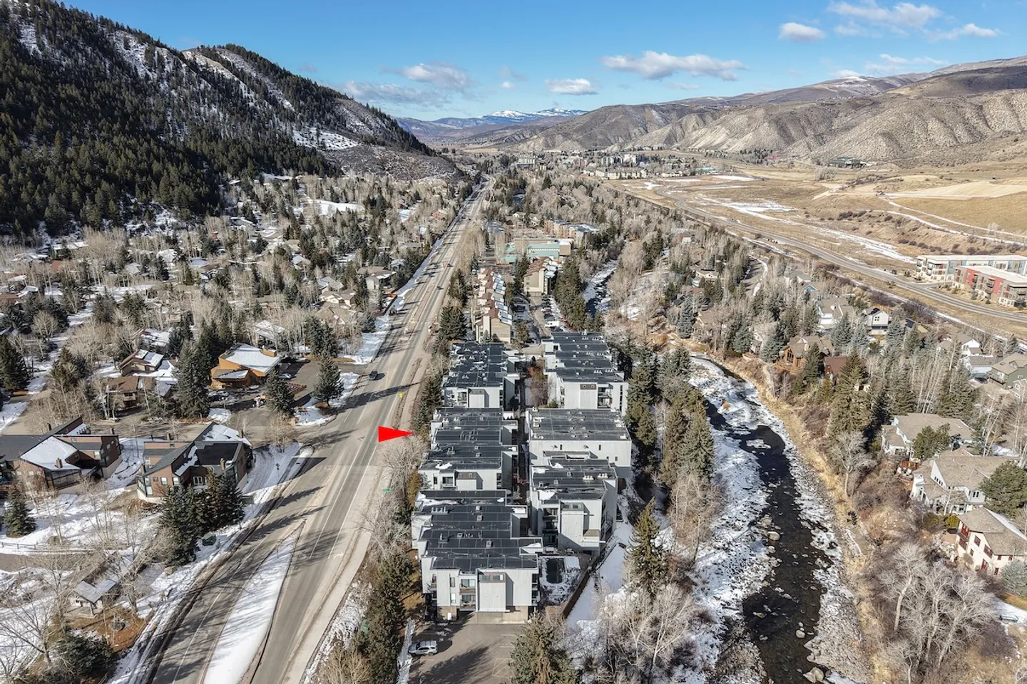 Aerial view of a contemporary townhouse complex situated between a road and a river in a mountain valley.