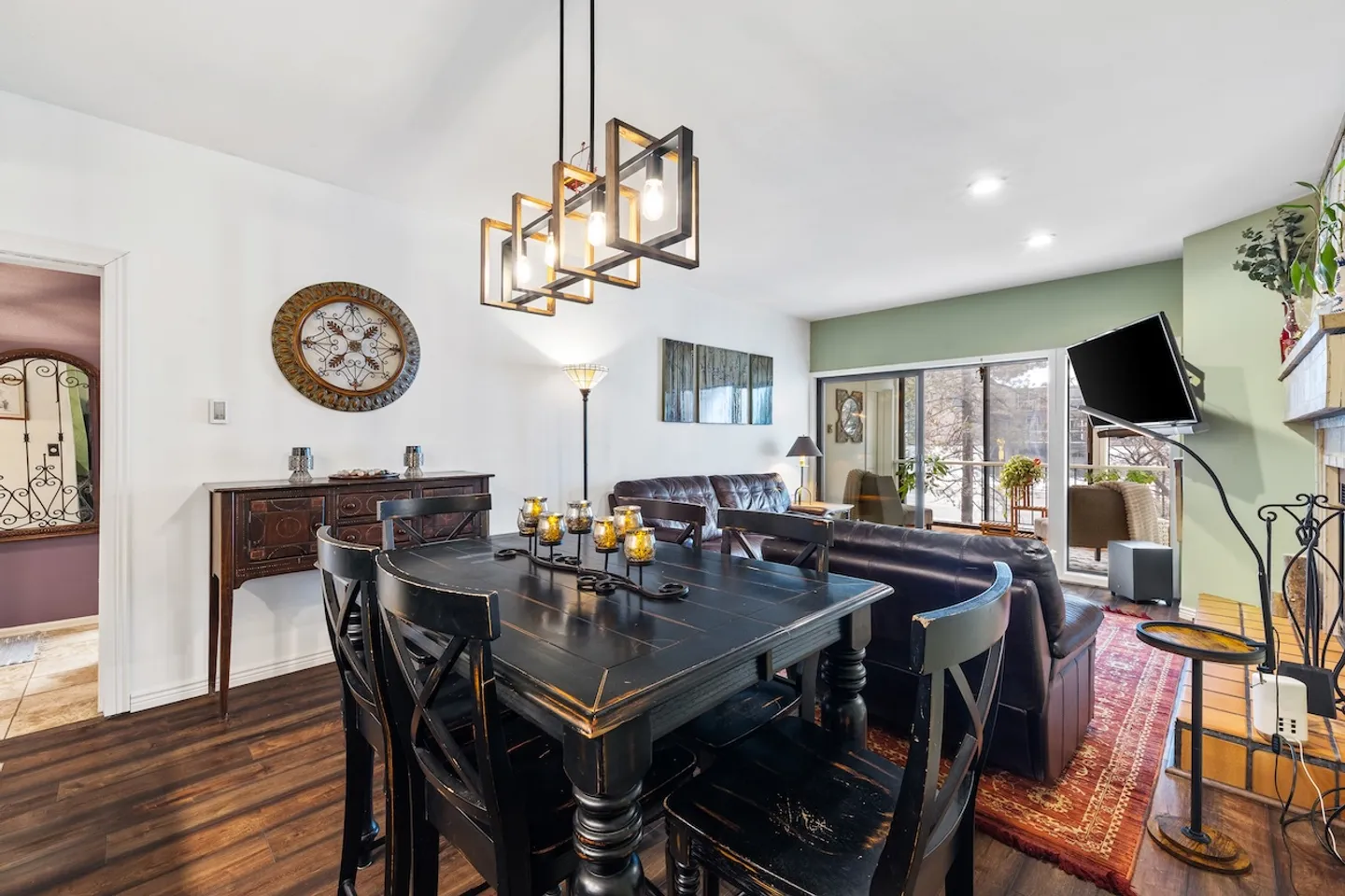 Dining area with a black wooden dining table and chairs, illuminated by a modern pendant light, adjacent to an open living area.