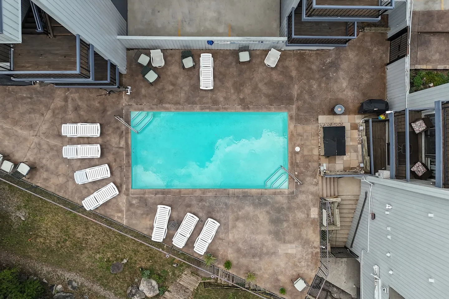 Aerial overhead view of an outdoor swimming pool surrounded by a patio with lounge chairs and buildings.